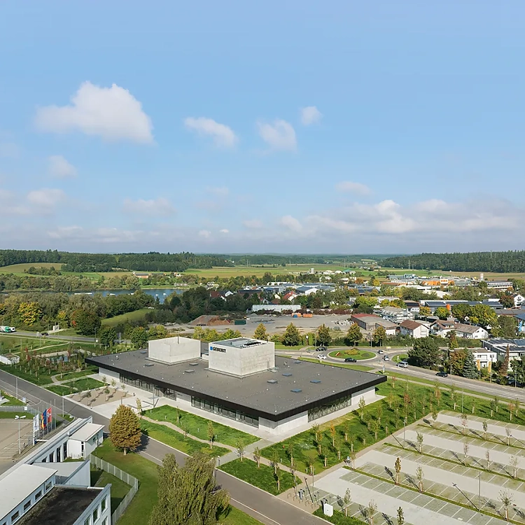 Der Geberit Campus ist als Pavillon konzipiert, reduziert auf Boden, Kuben und ein weit auskragendes Dach. Die drei große, zentralen Kuben stoßen durch die Dachfläche und markieren die zentralen Kompetenzfelder des Unternehmens. Sie sind von außen weithin sichtbar.